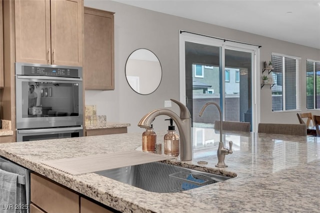 kitchen featuring double oven, sink, light stone countertops, and light brown cabinetry