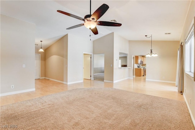 unfurnished living room with high vaulted ceiling, ceiling fan with notable chandelier, and light carpet