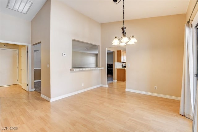 unfurnished dining area featuring a notable chandelier, a towering ceiling, and light hardwood / wood-style floors