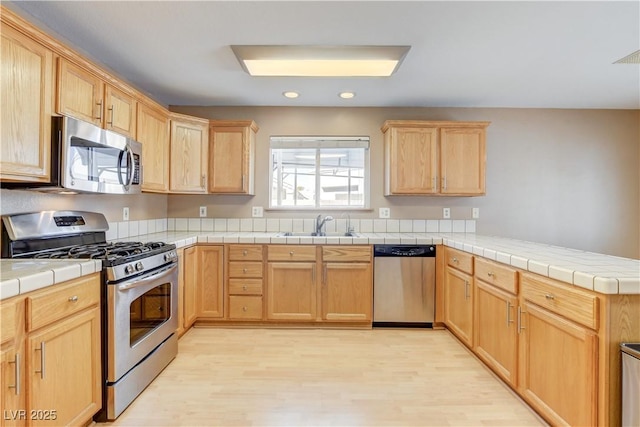 kitchen featuring sink, appliances with stainless steel finishes, tile counters, kitchen peninsula, and light wood-type flooring