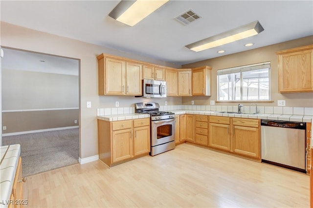 kitchen featuring appliances with stainless steel finishes, light brown cabinetry, sink, tile counters, and light hardwood / wood-style floors