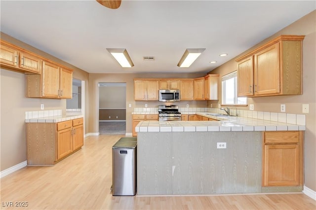 kitchen with sink, tile countertops, light wood-type flooring, appliances with stainless steel finishes, and kitchen peninsula