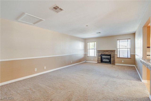 unfurnished living room featuring a stone fireplace and carpet flooring