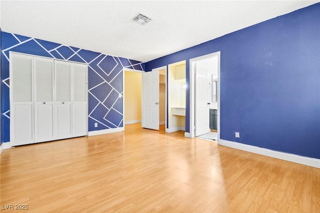 unfurnished bedroom with ensuite bath and wood-type flooring