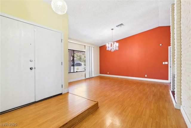 entrance foyer featuring an inviting chandelier, hardwood / wood-style flooring, vaulted ceiling, and a textured ceiling