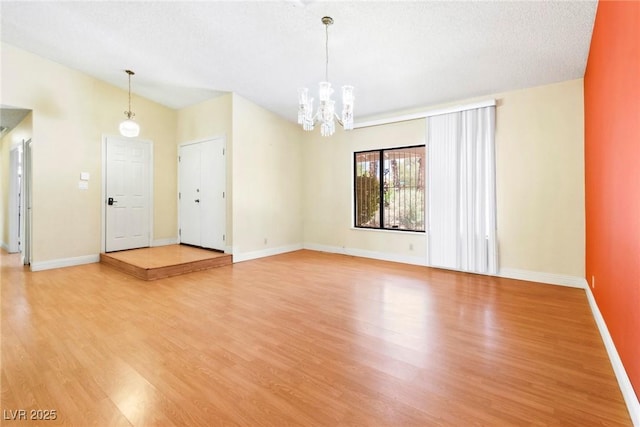 spare room with an inviting chandelier, wood-type flooring, lofted ceiling, and a textured ceiling