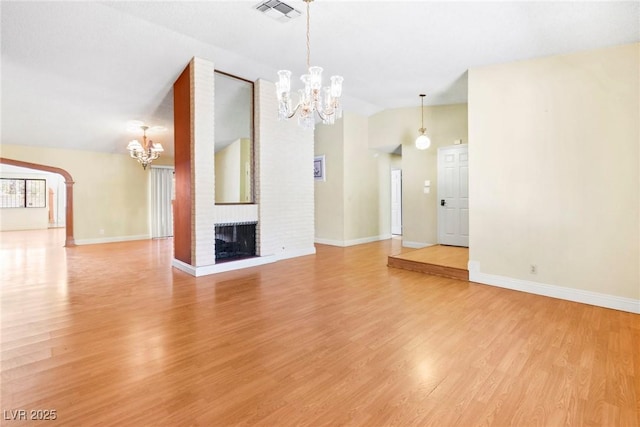 unfurnished living room with vaulted ceiling, a fireplace, an inviting chandelier, and light hardwood / wood-style flooring