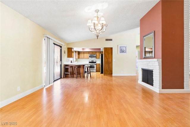 unfurnished living room featuring vaulted ceiling, an inviting chandelier, a fireplace, and light hardwood / wood-style floors