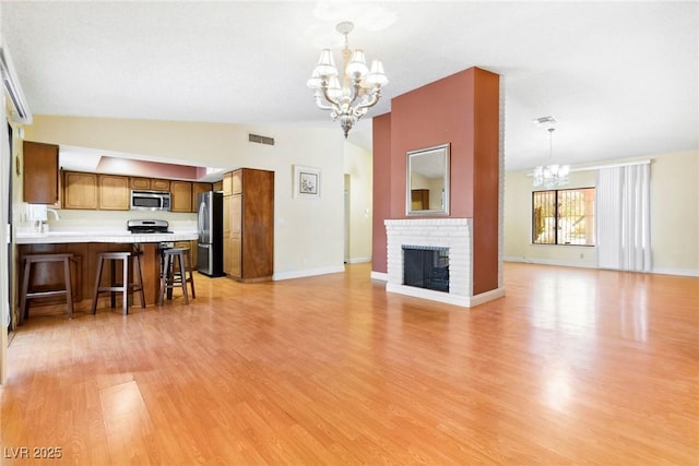 living room with lofted ceiling, a brick fireplace, light hardwood / wood-style flooring, and a chandelier