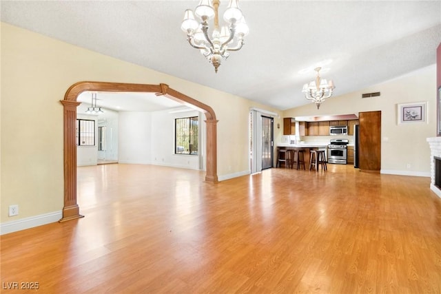 unfurnished living room featuring vaulted ceiling, plenty of natural light, light wood-type flooring, and a chandelier