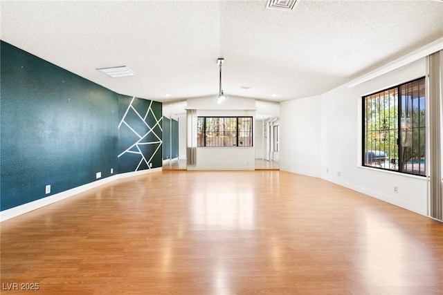 spare room featuring vaulted ceiling, a textured ceiling, and light wood-type flooring