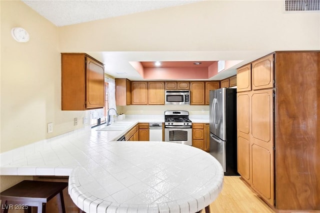 kitchen featuring stainless steel appliances, sink, tile counters, and kitchen peninsula