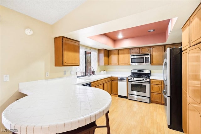 kitchen featuring kitchen peninsula, sink, tile counters, a tray ceiling, and stainless steel appliances