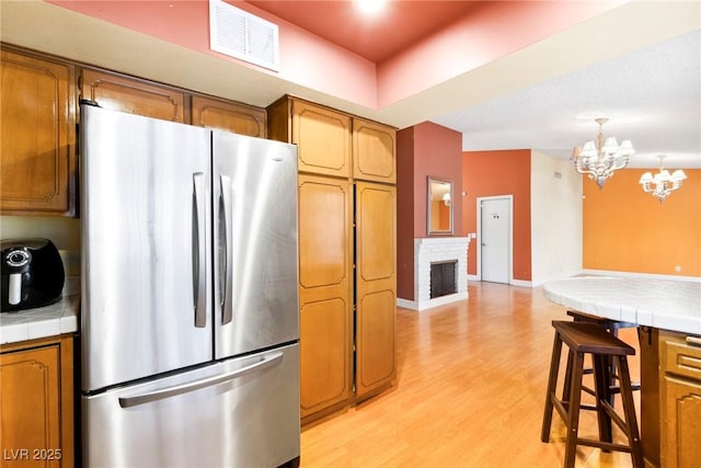 kitchen with light hardwood / wood-style flooring, stainless steel fridge, a brick fireplace, decorative light fixtures, and tile countertops