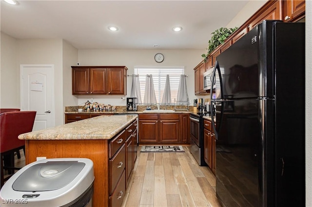 kitchen featuring a kitchen island, appliances with stainless steel finishes, sink, light stone countertops, and light wood-type flooring