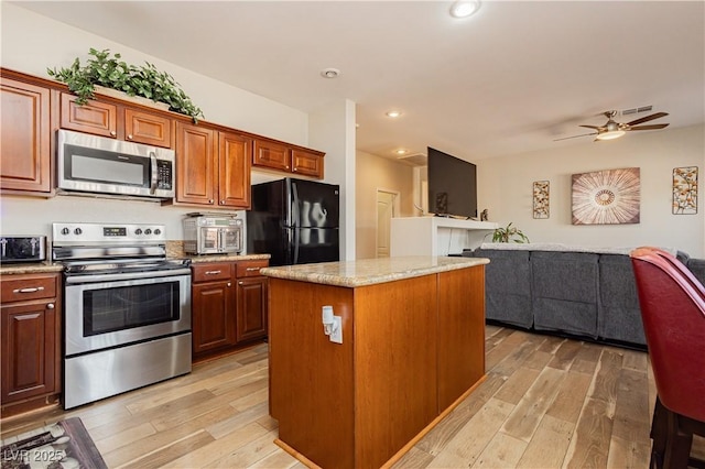 kitchen featuring ceiling fan, appliances with stainless steel finishes, a center island, light stone countertops, and light wood-type flooring