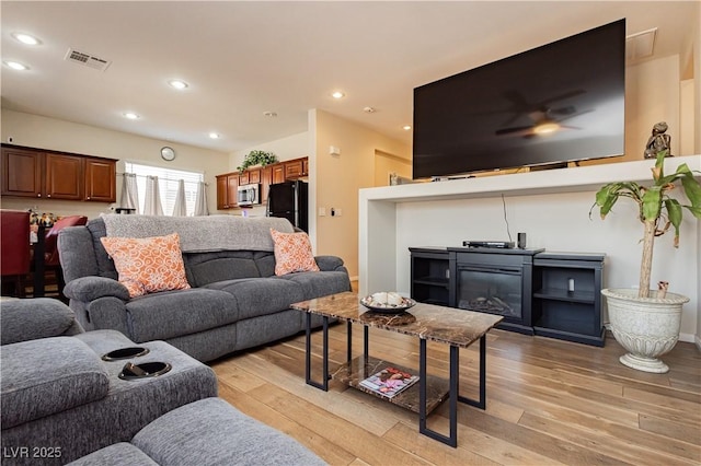 living room with light wood-type flooring, visible vents, a glass covered fireplace, and recessed lighting