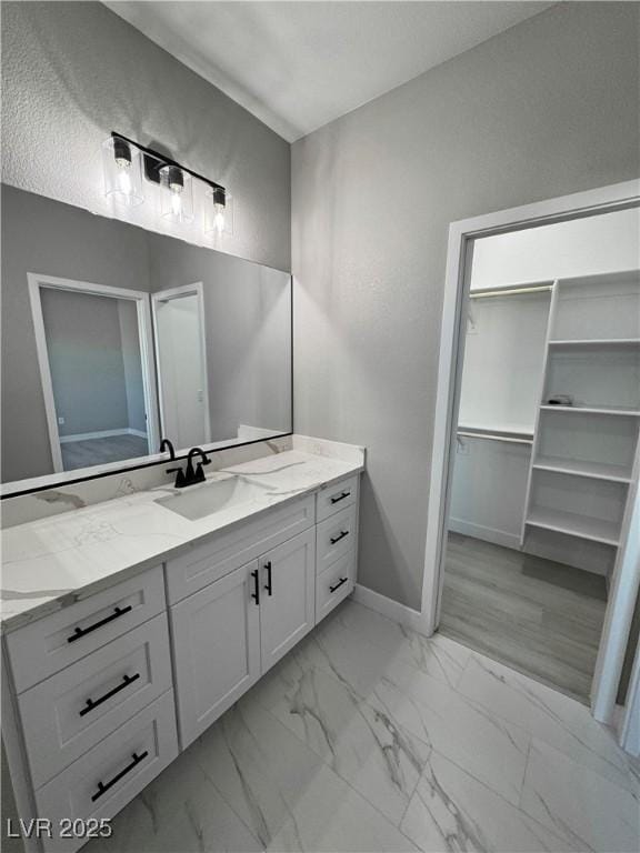 bathroom featuring marble finish floor, a spacious closet, baseboards, and vanity