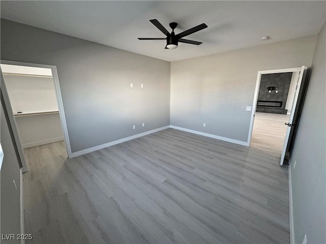 unfurnished bedroom featuring light wood-style flooring, a spacious closet, baseboards, and ceiling fan