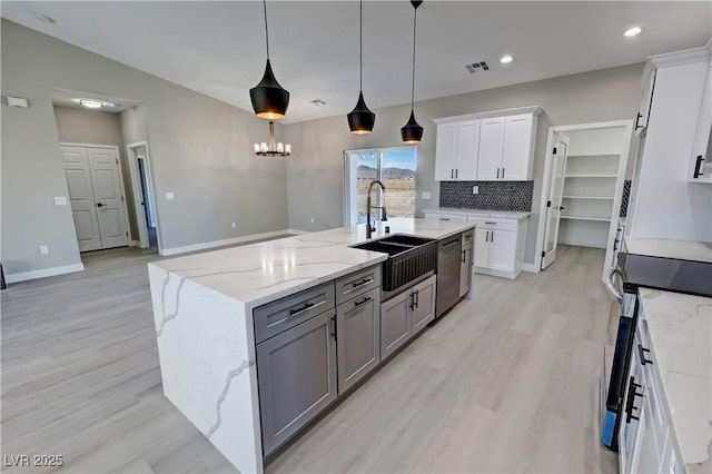 kitchen featuring hanging light fixtures, a kitchen island with sink, white cabinetry, a sink, and light stone countertops