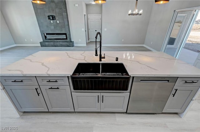 kitchen featuring light stone counters, gray cabinets, hanging light fixtures, and stainless steel dishwasher