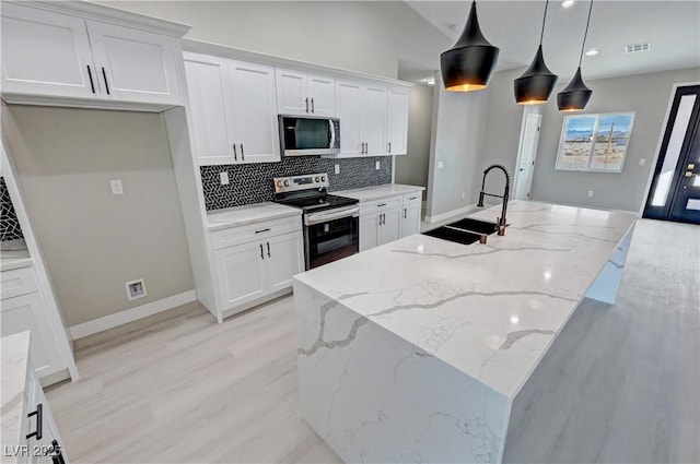 kitchen with appliances with stainless steel finishes, a center island with sink, decorative light fixtures, and white cabinetry