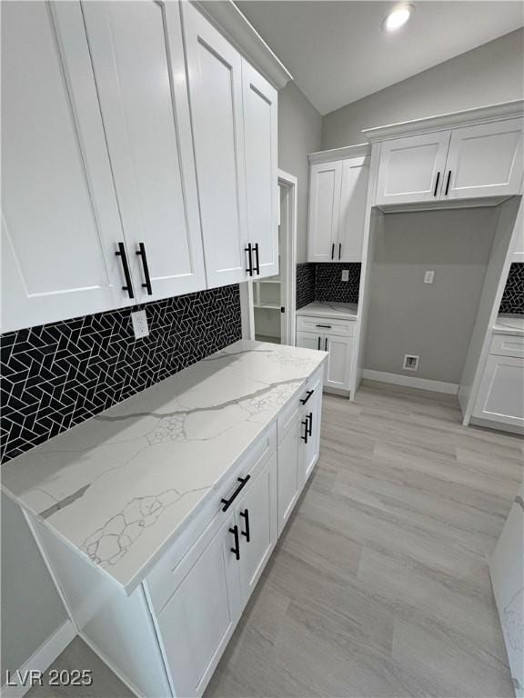 kitchen with light stone countertops, tasteful backsplash, vaulted ceiling, and white cabinets