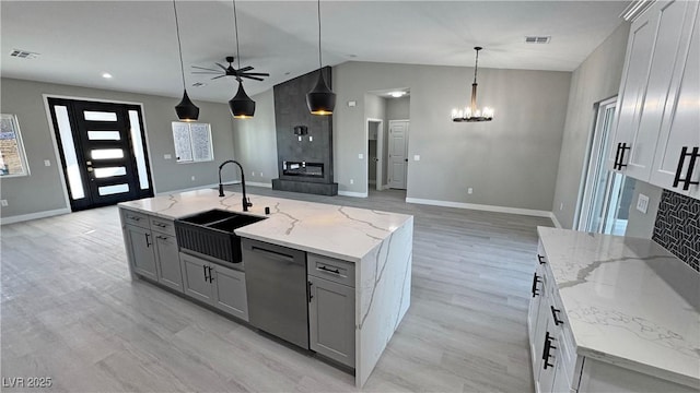 kitchen with black dishwasher, an island with sink, hanging light fixtures, light stone countertops, and a sink