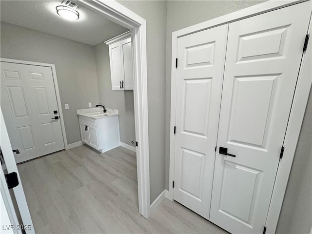 clothes washing area with light wood-style floors, baseboards, and a sink