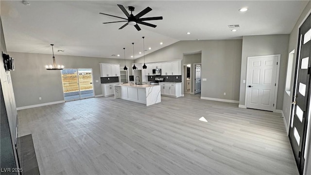 kitchen featuring pendant lighting, a center island with sink, light countertops, open floor plan, and white cabinetry