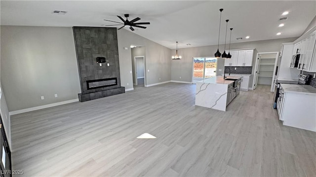 kitchen featuring a kitchen island with sink, white cabinets, a tiled fireplace, and open floor plan