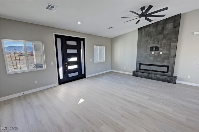 entryway featuring ceiling fan, a tile fireplace, light wood-style flooring, visible vents, and baseboards