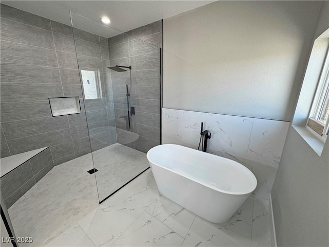 bathroom with marble finish floor, a freestanding tub, tile walls, and walk in shower