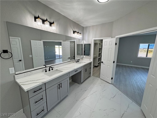 full bath with double vanity, marble finish floor, baseboards, and a sink