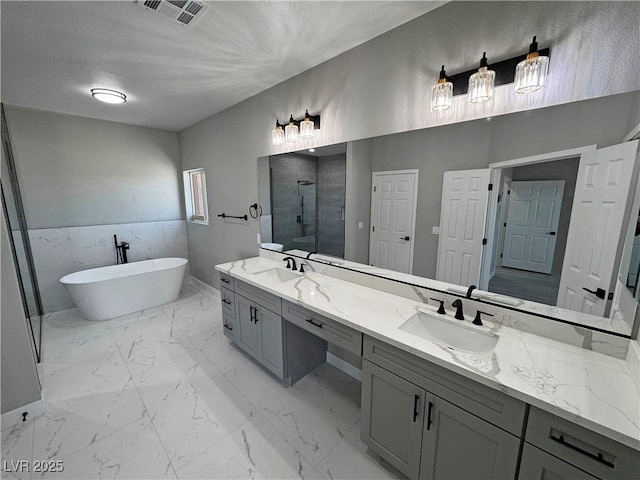 bathroom with marble finish floor, visible vents, a sink, and a soaking tub