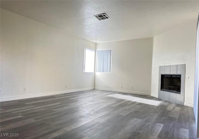 unfurnished living room with a tiled fireplace, a textured ceiling, and dark hardwood / wood-style flooring