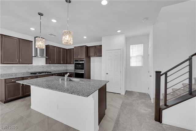 kitchen featuring stainless steel appliances, light stone countertops, decorative backsplash, a center island with sink, and decorative light fixtures