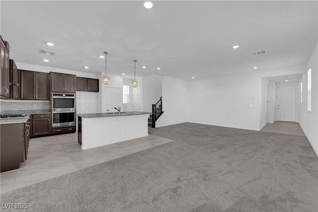 kitchen with a center island with sink, appliances with stainless steel finishes, light colored carpet, and hanging light fixtures