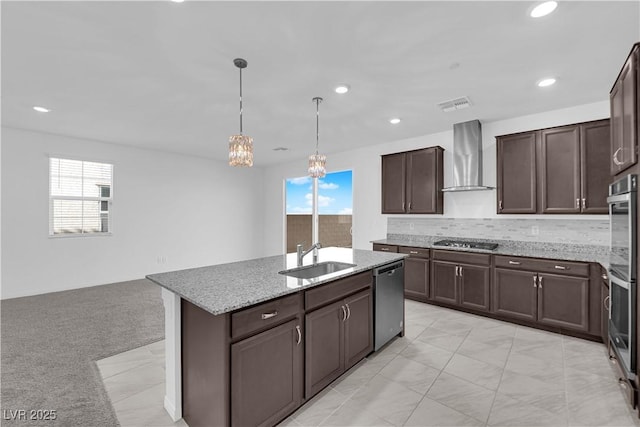 kitchen with appliances with stainless steel finishes, an island with sink, sink, dark brown cabinets, and wall chimney exhaust hood