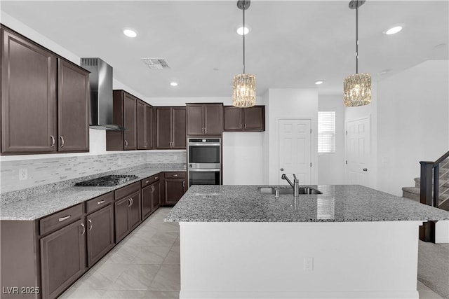 kitchen featuring wall chimney range hood, hanging light fixtures, sink, and appliances with stainless steel finishes