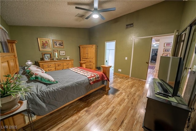 bedroom featuring ceiling fan, lofted ceiling, a textured ceiling, and light hardwood / wood-style floors