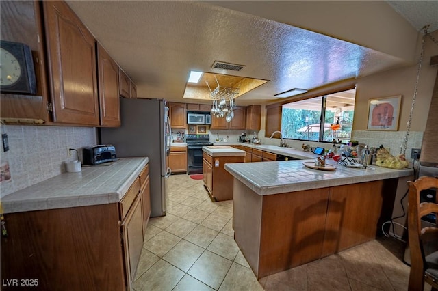 kitchen with sink, hanging light fixtures, kitchen peninsula, stainless steel appliances, and a textured ceiling