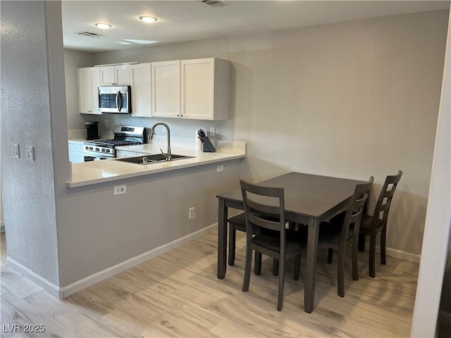 kitchen featuring sink, white cabinetry, light hardwood / wood-style flooring, kitchen peninsula, and stainless steel appliances