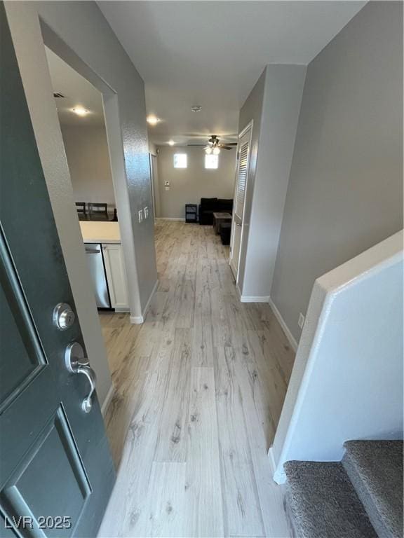 corridor with light wood-type flooring, stairs, and baseboards