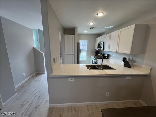 kitchen featuring sink, light hardwood / wood-style flooring, white cabinetry, stainless steel appliances, and kitchen peninsula