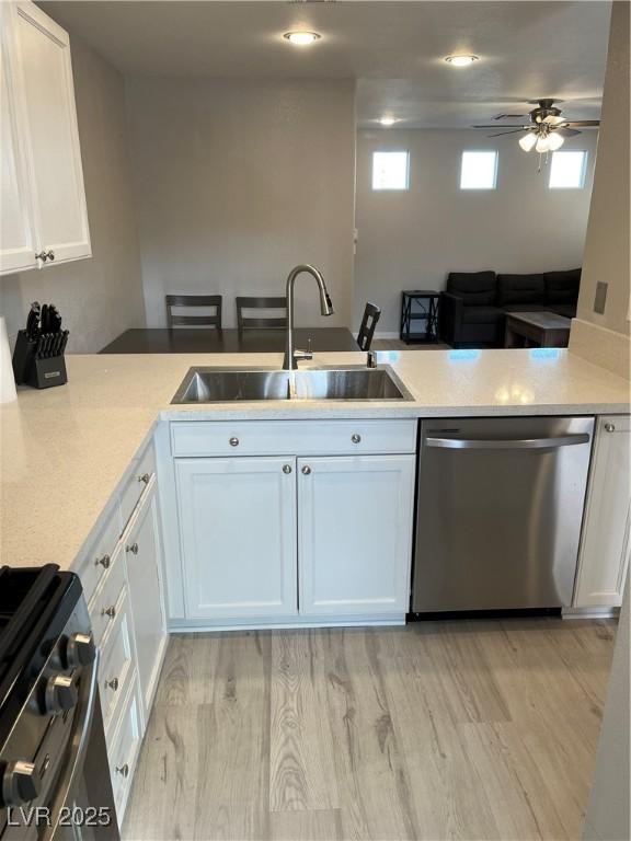 kitchen with light wood finished floors, stainless steel appliances, light countertops, white cabinetry, and a sink