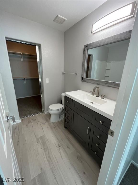 bathroom featuring toilet, wood finished floors, visible vents, vanity, and a walk in closet