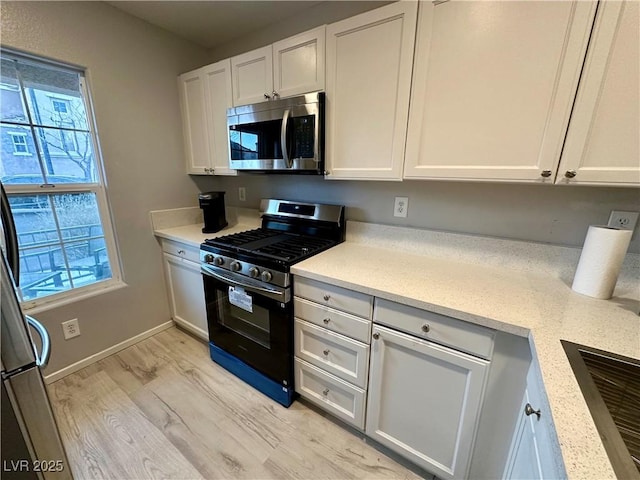 kitchen with light wood finished floors, baseboards, white cabinets, range with gas cooktop, and stainless steel microwave