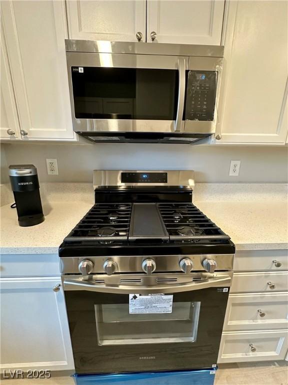 kitchen featuring appliances with stainless steel finishes, white cabinets, and light stone counters