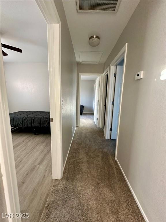 hallway featuring attic access, visible vents, baseboards, and carpet flooring